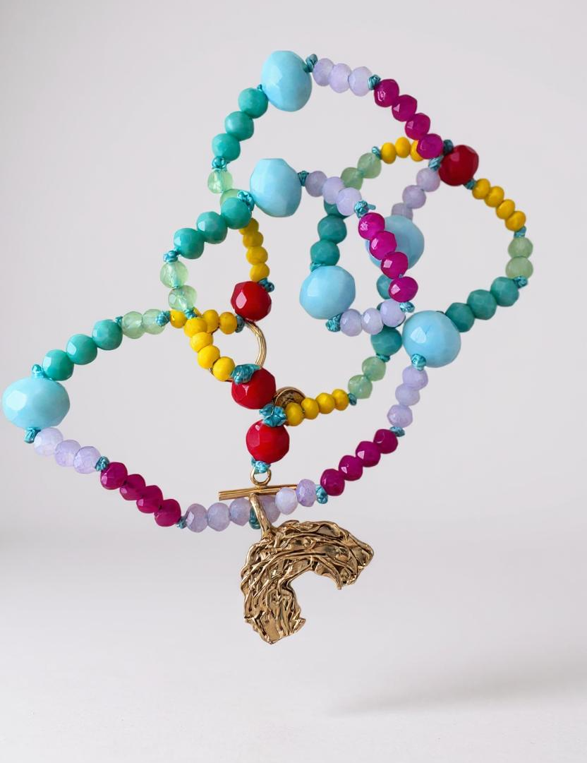 collar  de cuentas de cristales multicolor con un dije dorado en forma de arcoíris sobre fondo blanco.