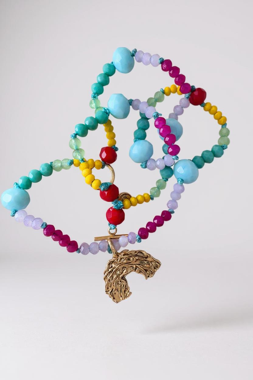 collar de cuentas de cristales multicolor con un dije dorado en forma de arcoíris sobre fondo blanco.