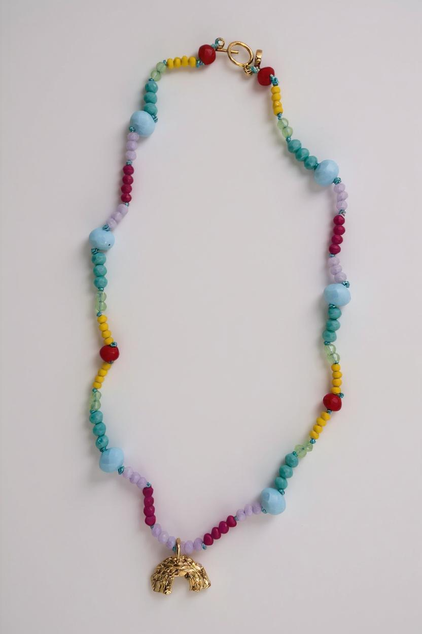 Collar de cuentas de colores con un colgante dorado sobre fondo gris claro.