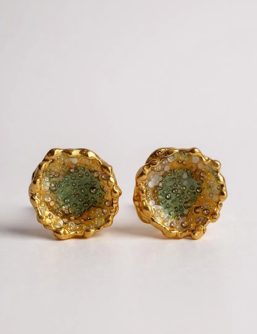 Disposición plana de un par de aretes Topos Coca M en bronce bañado en oro, pintados a mano en verde sage con granulación de vidrio, sobre fondo blanco.