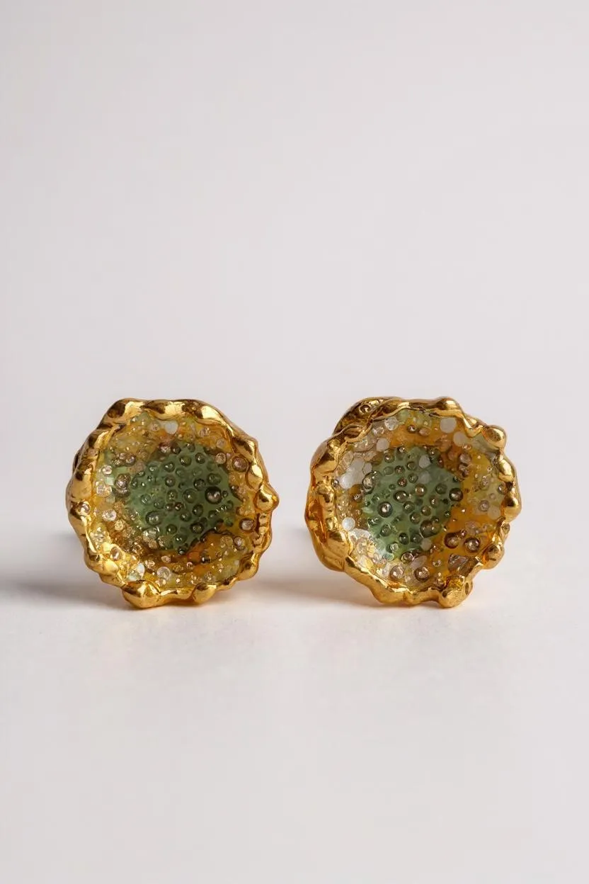 Disposición plana de un par de aretes Topos Coca M en bronce bañado en oro, pintados a mano en verde sage con granulación de vidrio, sobre fondo blanco.