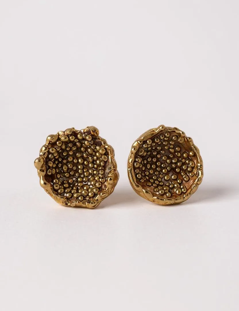 Disposición plana de un par de aretes Topos Coca M en bronce bañado en oro, pintados a mano en rust con granulación de vidrio, sobre fondo blanco.