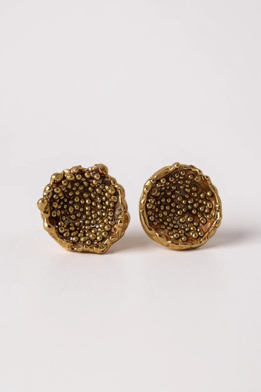 Disposición plana de un par de aretes Topos Coca M en bronce bañado en oro, pintados a mano en rust con granulación de vidrio, sobre fondo blanco.