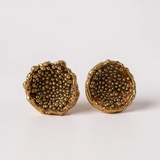 Disposición plana de un par de aretes Topos Coca M en bronce bañado en oro, pintados a mano en rust con granulación de vidrio, sobre fondo blanco.