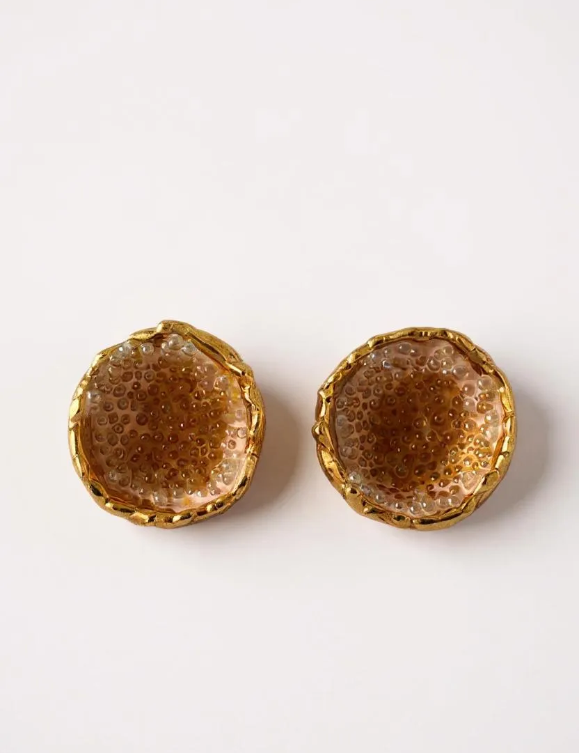 Disposición plana de un par de aretes Topos Coca M en bronce bañado en oro, pintados a mano en tono sunset con granulación de vidrio turquesa, sobre fondo blanco.