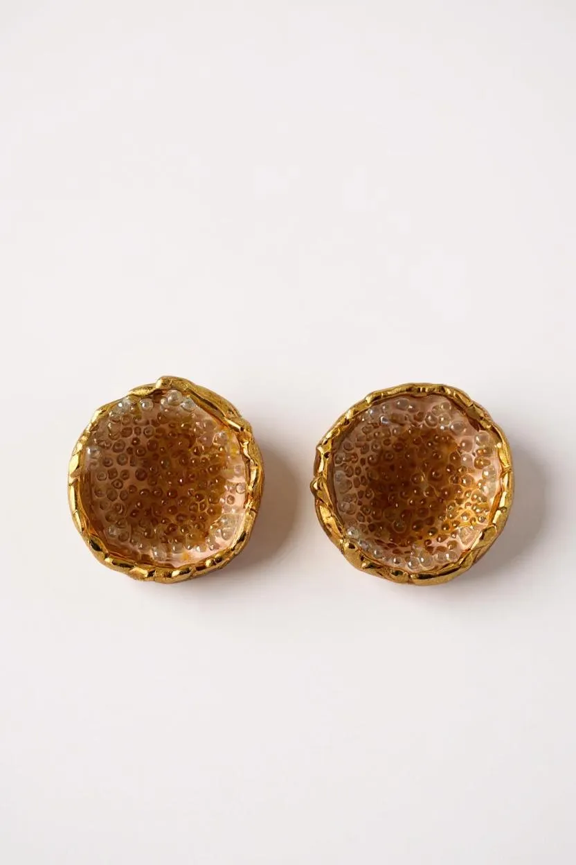 Disposición plana de un par de aretes Topos Coca M en bronce bañado en oro, pintados a mano en tono sunset con granulación de vidrio turquesa, sobre fondo blanco.