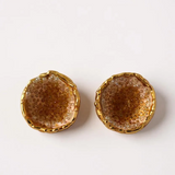 Disposición plana de un par de aretes Topos Coca M en bronce bañado en oro, pintados a mano en tono sunset con granulación de vidrio turquesa, sobre fondo blanco.