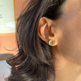 Primer plano lateral de la oreja de una mujer con un Topos Coca M en sage pintado a mano con granulación de vidrio en montura de bronce bañado en oro, cabello recogido, sobre fondo neutro.