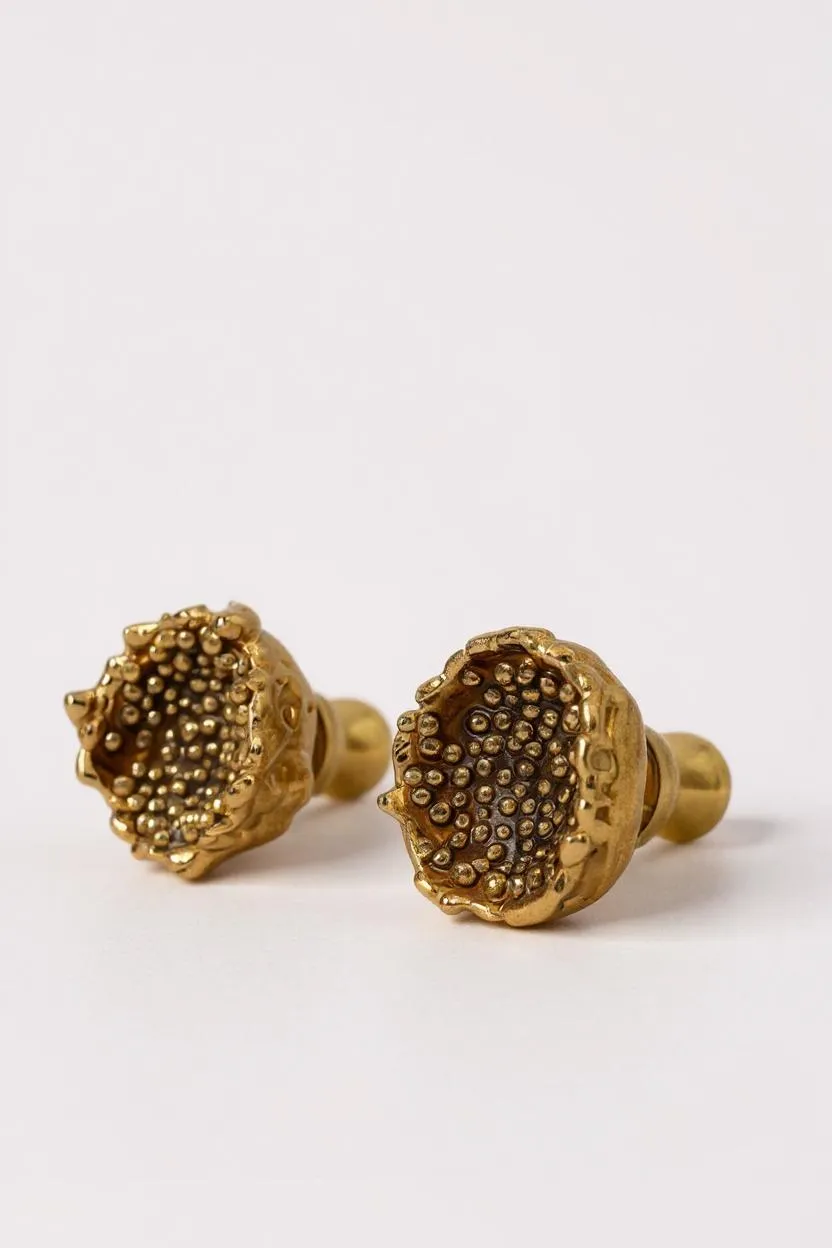 Primer plano de dos aretes Topos Coca M en bronce bañado en oro con textura de granulación en vidrio detallada, sobre un fondo neutro claro.