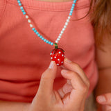 Persona que lleva un collar con un colgante de fresa, sosteniéndolo en la mano.