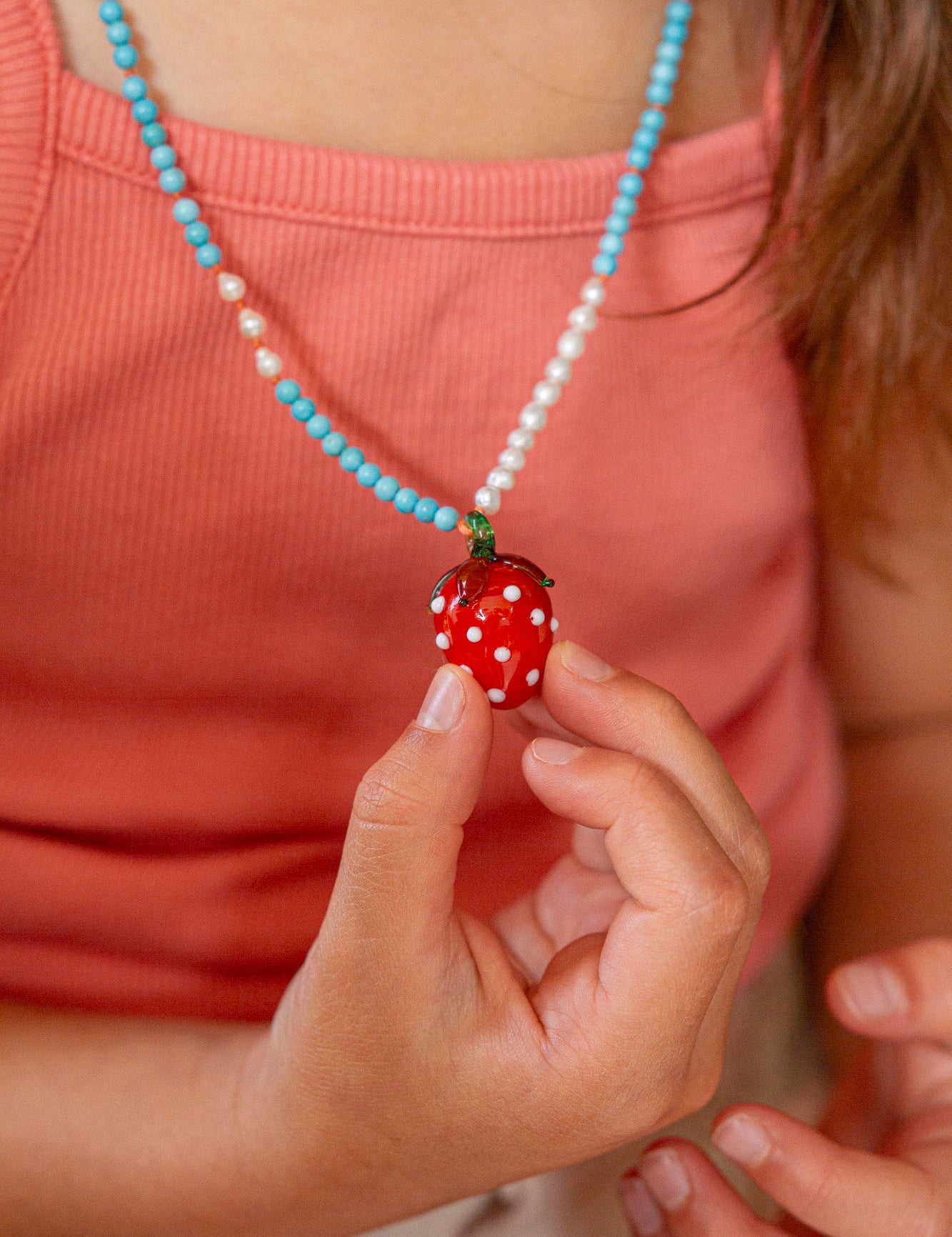 Persona que lleva un collar con un colgante de fresa, sosteniéndolo en la mano.
