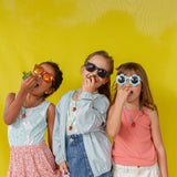 Tres niñas juntas frente a una pared amarilla, cada una lleva el Collar Fresa con el colgante colgando a distintas alturas.