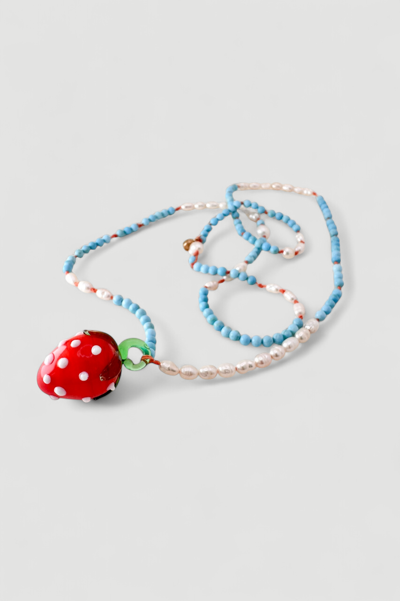 Collar Fresa dispuesto verticalmente sobre fondo blanco, mostrando cuentas alternadas turquesas y blancas y un colgante de fresa de vidrio rojo.