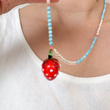 Primer plano del torso de una niña con camiseta sin mangas blanca y el Collar Fresa, con el colgante de fresa rojo centrado.