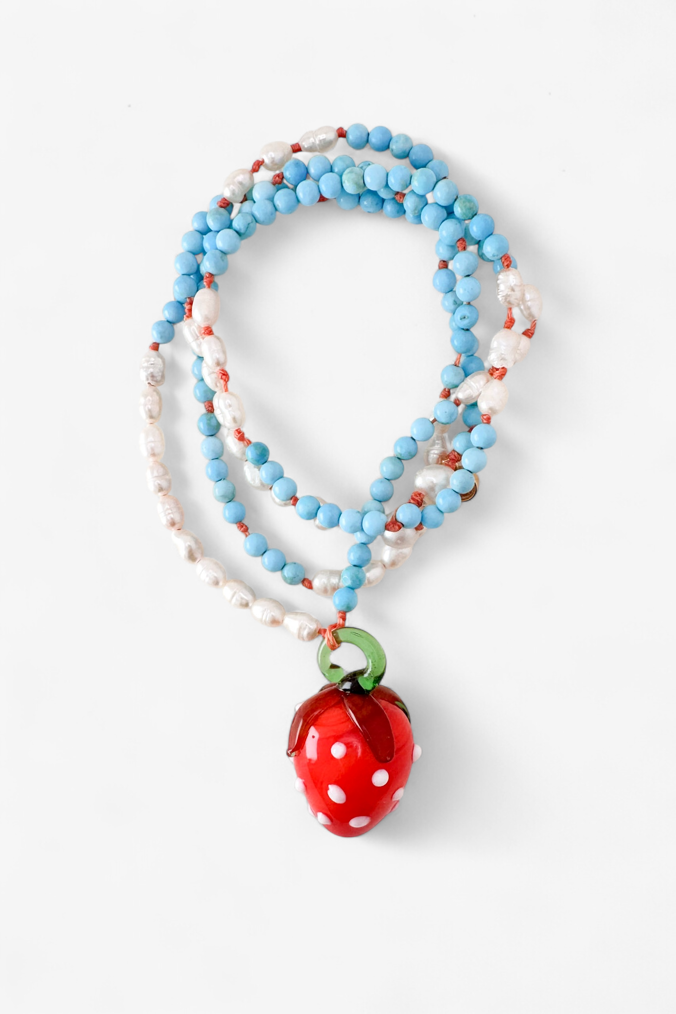 Coiled Strawberry Necklace on a white background, showcasing multiple loops of turquoise and white beads with the red glass strawberry pendant in view