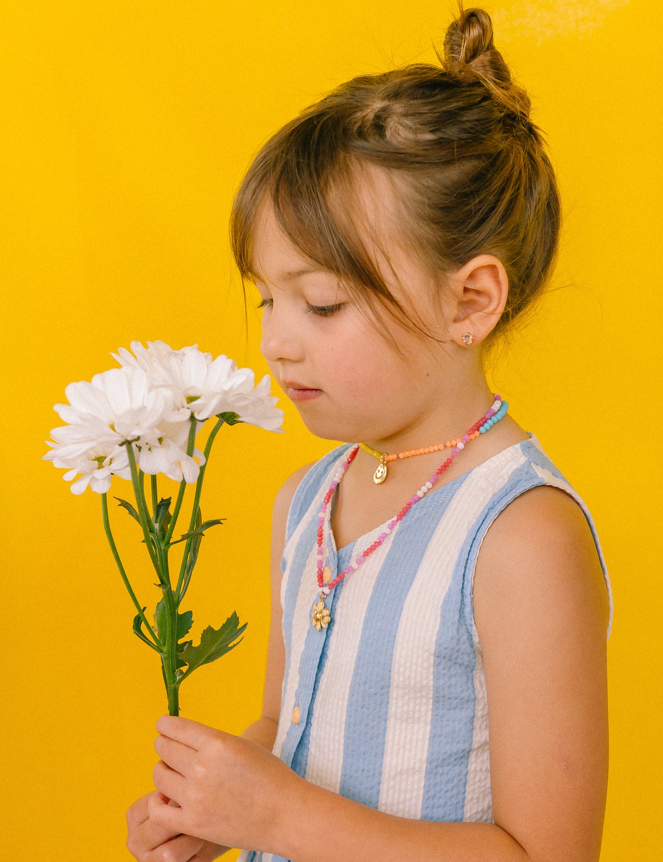 niña con vestido azul claro usando el Collar Margarita artesanal con dije dorado y cadena de cristales rosa.