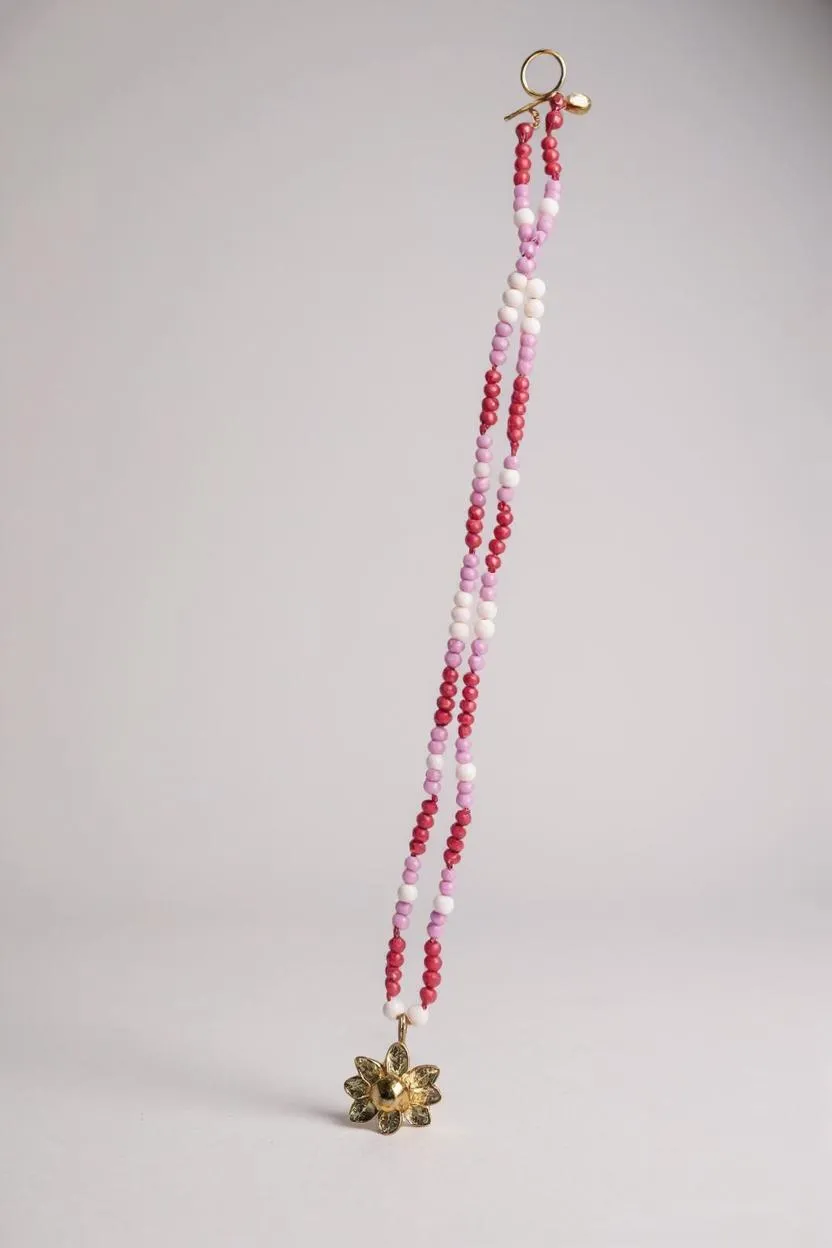 Collar Margarita extendido, con dije dorado en forma de flor y cadena de cristales rosa, fucsia y blanco.