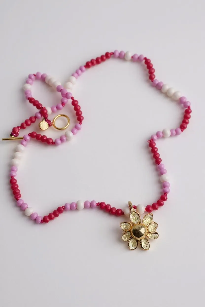 Collar Margarita artesanal con dije dorado en forma de flor, dispuesto en círculo sobre fondo blanco.
