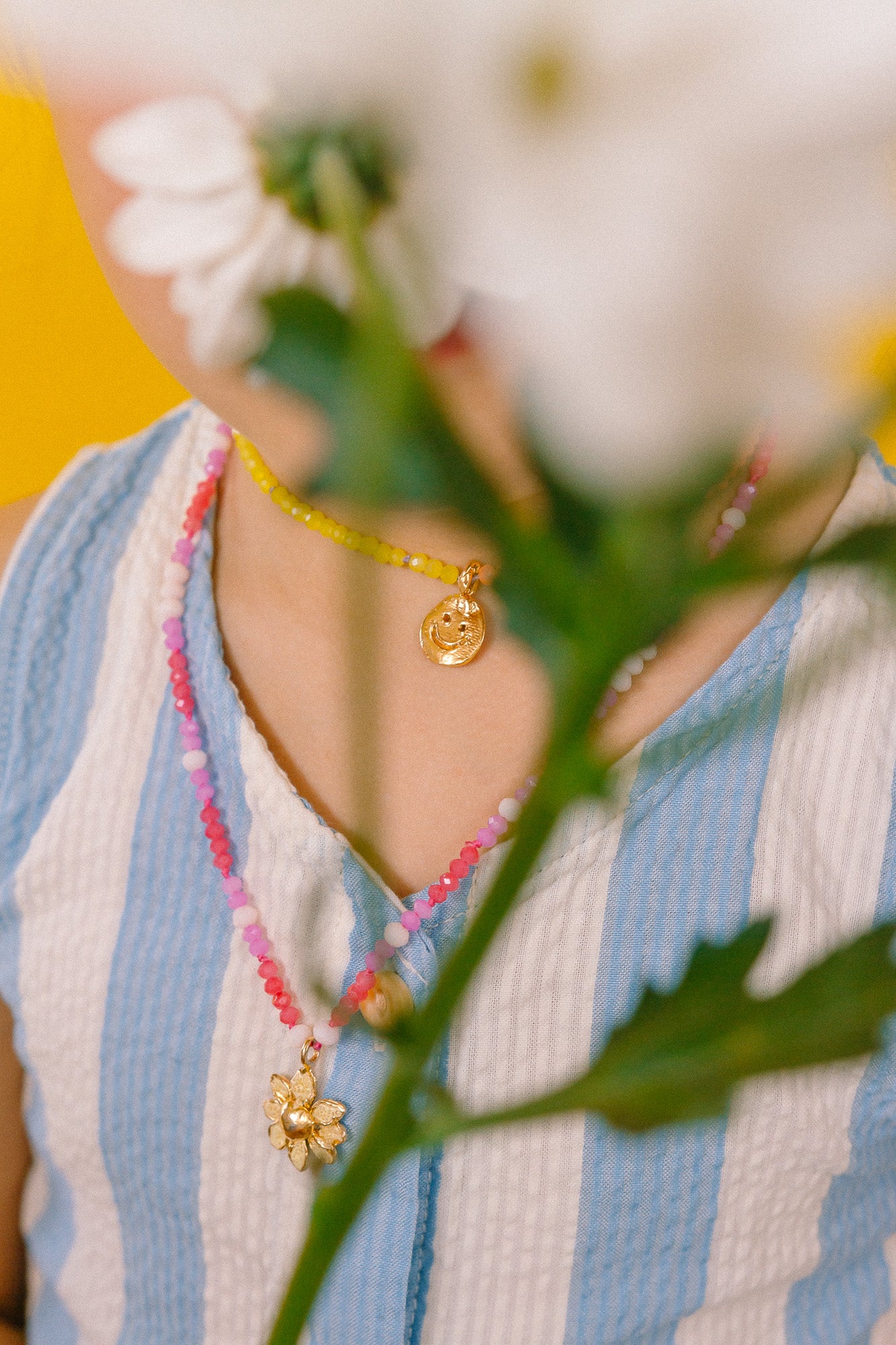 Detalle del dije dorado del Collar Margarita rodeado de cristales rosa, blanco y fucsia.