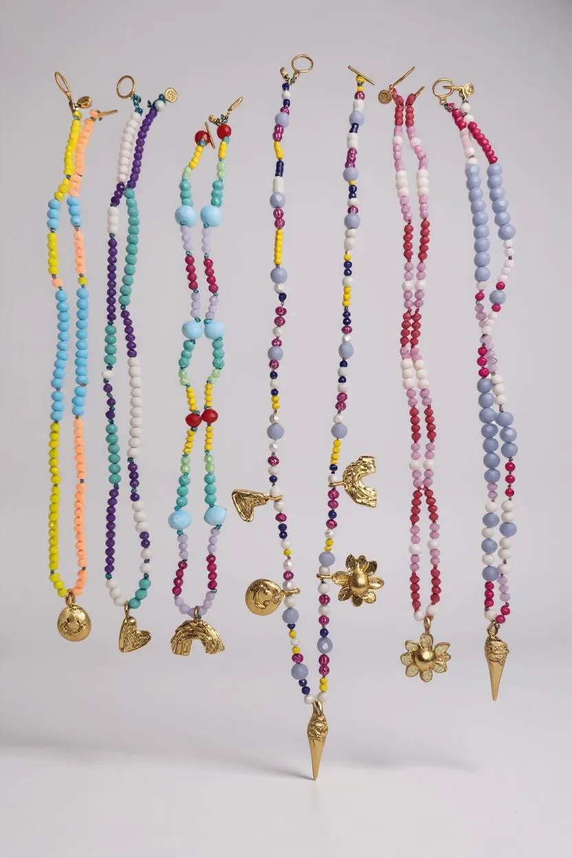 Conjunto de collares de cuentas de colores con varios colgantes sobre un fondo gris claro.