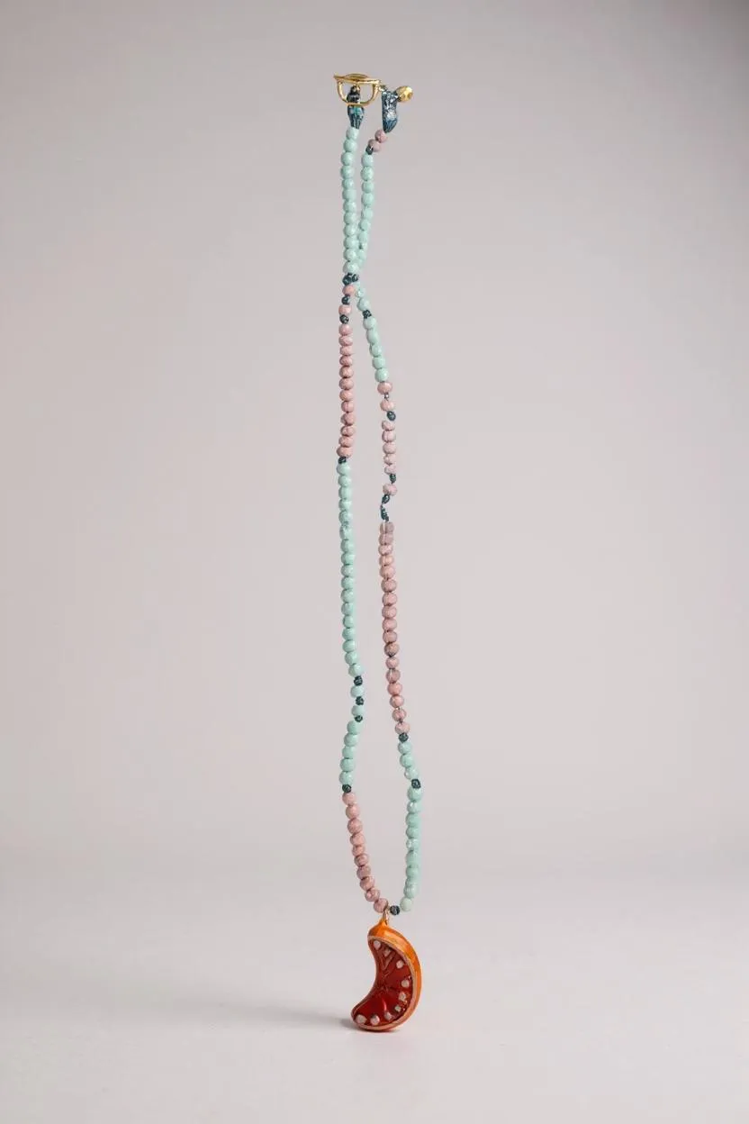 Collar Naranja extendido verticalmente sobre fondo blanco, mostrando la cadena completa de cuentas en verde menta y rosa y el colgante de media luna naranja en la parte inferior.