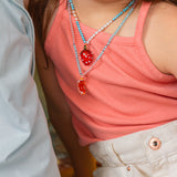 Primer plano del torso de una niña con camiseta coral y pantalones blancos, con el colgante del Collar Naranja a la altura del pecho.