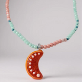 Collar Naranja enrollado sobre fondo blanco, mostrando varias vueltas de cuentas en verde menta y rosa con el colgante de media luna naranja visible.