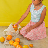 Niña arrodillada en el suelo con blusa verde menta y falda pastel juega con naranjas y lleva puesto el Collar Naranja