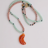 Primer plano del Collar Naranja colgando alrededor del cuello de una camiseta blanca, con el colgante de media luna naranja centrado