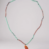 Collar Naranja dispuesto en una suave curva sobre superficie blanca, resaltando las cuentas en verde menta y rosa y el colgante de media luna naranja.