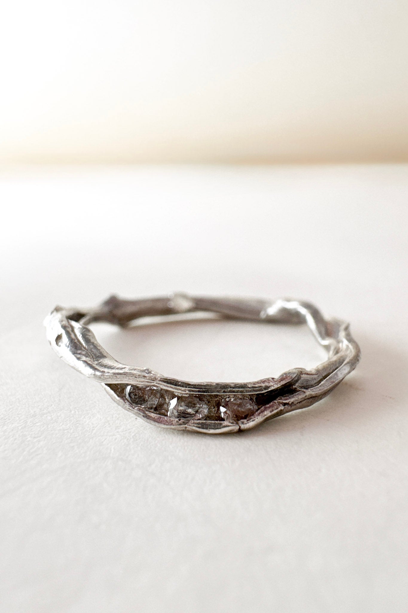 Anillo artesanal de plata con diamantes de laboratorio, diseño orgánico en forma de rama, colocado sobre una superficie blanca.