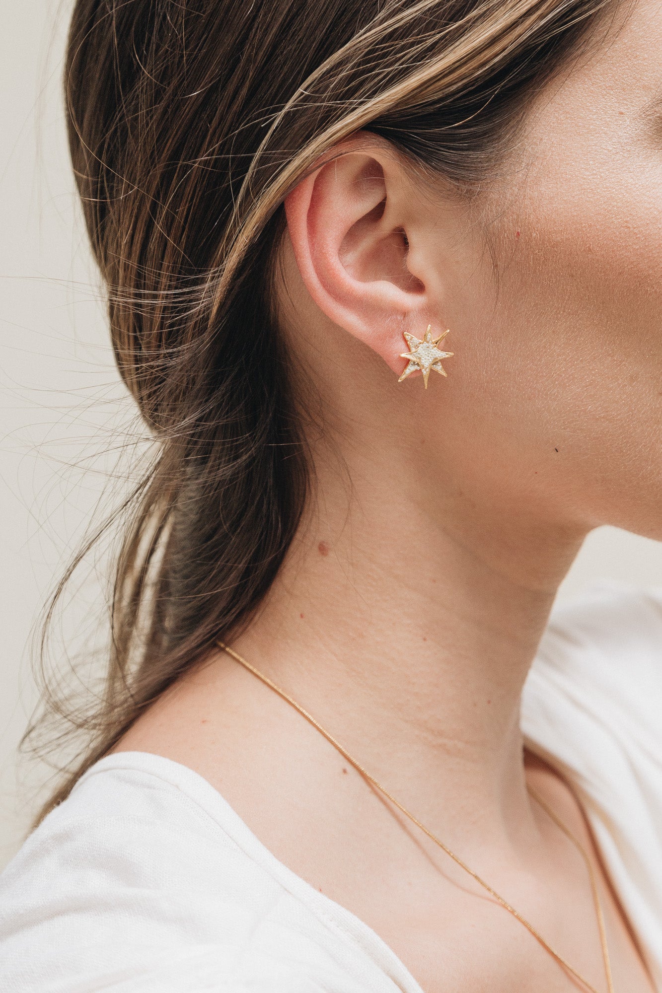 Primer plano lateral de la oreja de una mujer con el cabello recogido detrás, luciendo un arete topos de estrella bañados en oro.