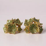 Par de aretes Galaxea en color sage: bañados en oro, con forma de galaxia y cúmulos de gránulos de vidrio verde salvia, sobre un fondo claro.