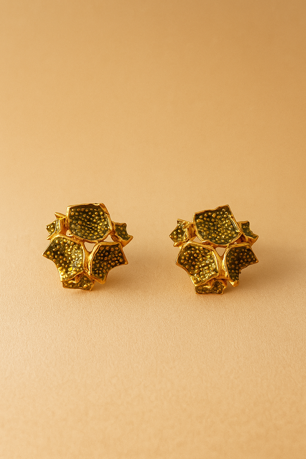 Dos aretes Galaxea en color sage: bañados en oro, con forma floral y gránulos de vidrio verde salvia, colocados lado a lado sobre un fondo beige cálido.