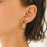 Primer plano lateral de la oreja de una mujer luciendo la variante Mostaza del Arete Lechuga, pintado a mano en amarillo mostaza con granulación de vidrio en montura de bronce bañado en oro, cabello recogido, sobre fondo neutro.