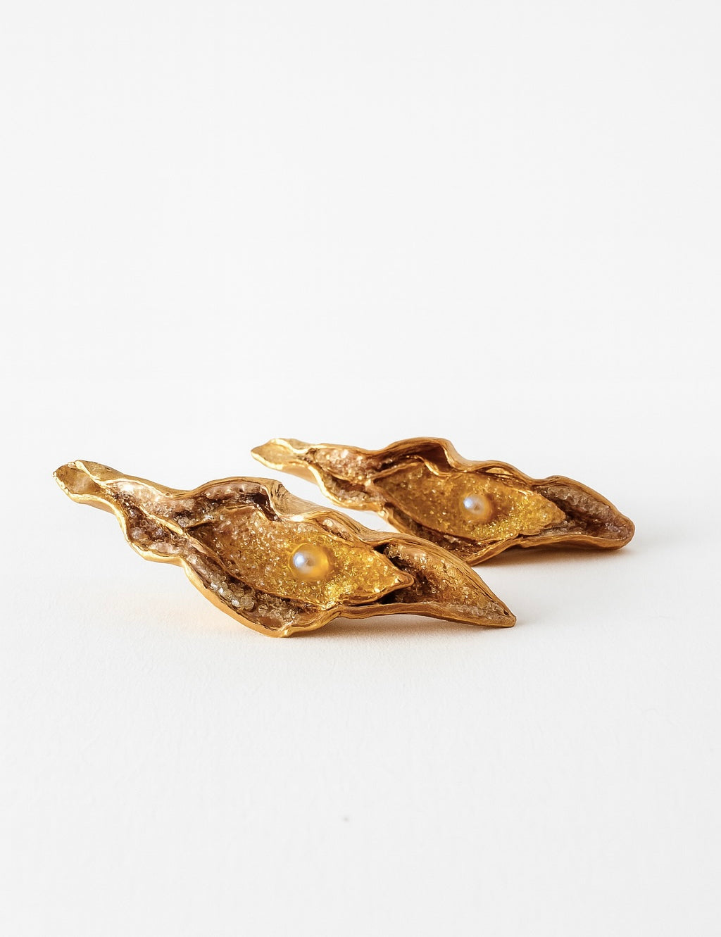 Disposición plana de dos Aretes Lechuga variante Mustard en bronce bañado en oro, pintados a mano en rust con granulación de vidrio, sobre fondo blanco.