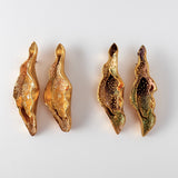 Disposición plana de cuatro Aretes Lechuga sobre fondo blanco—dos pintados a mano en amarillo mostaza y dos en rust, todos con granulación de vidrio y montura de bronce bañado en oro.