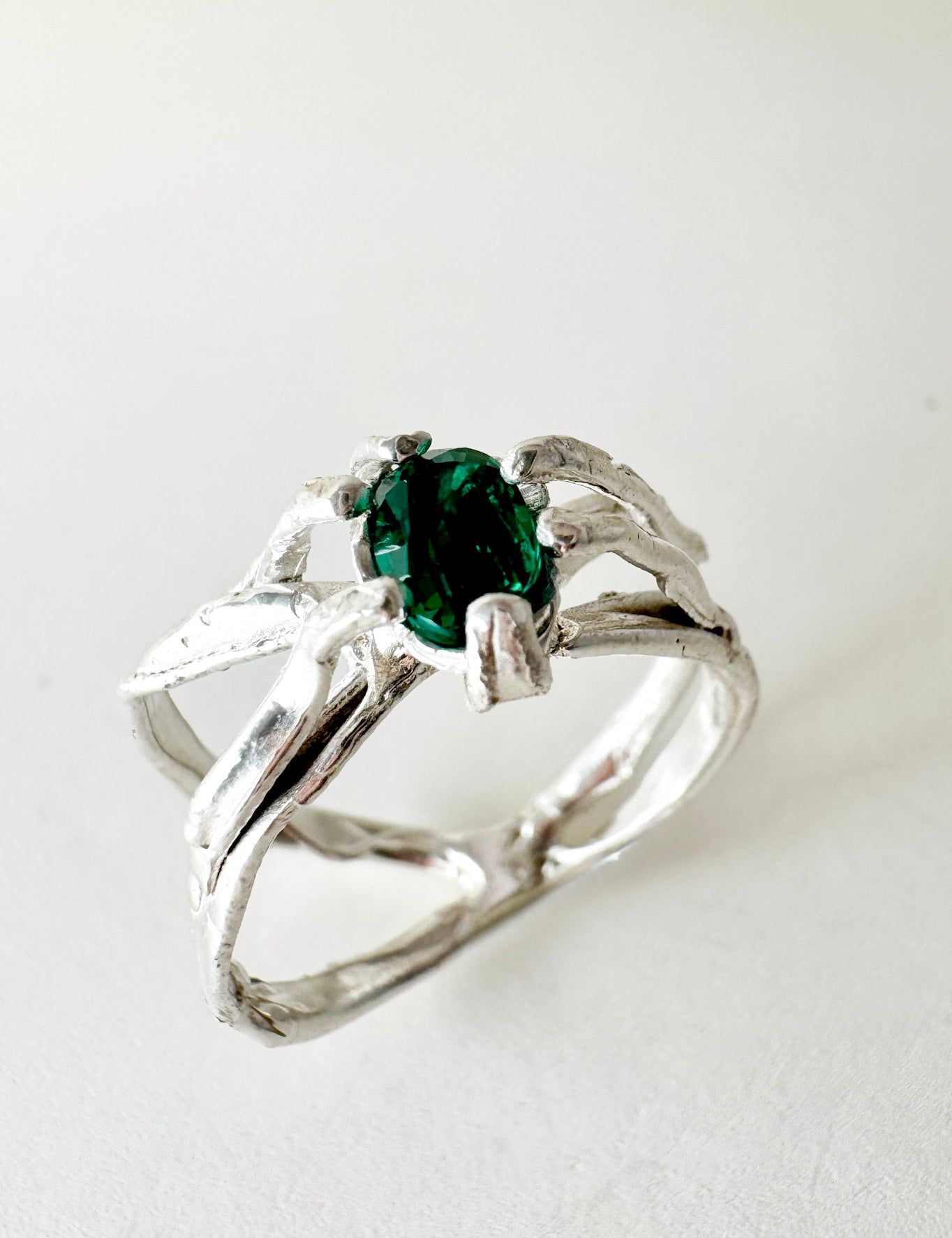 Anillo de plata esterlina con esmeralda de laboratorio engastada en banda orgánica esculpida, visto de frente sobre fondo neutro.