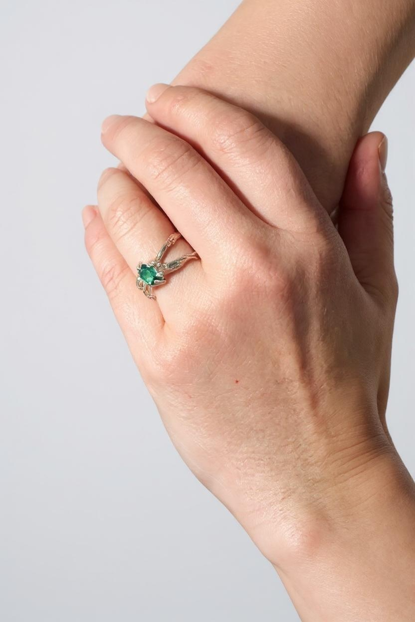 Anillo de plata con esmeralda de laboratorio puesto en una mano, fotografiado frente a una pared gris clara.