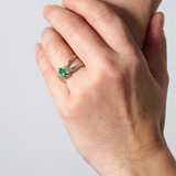 Anillo de plata con esmeralda de laboratorio puesto en una mano, fotografiado frente a una pared gris clara.