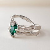 Vista frontal inclinada del anillo de plata esterlina con esmeralda de laboratorio verde intensa, sobre superficie blanca.