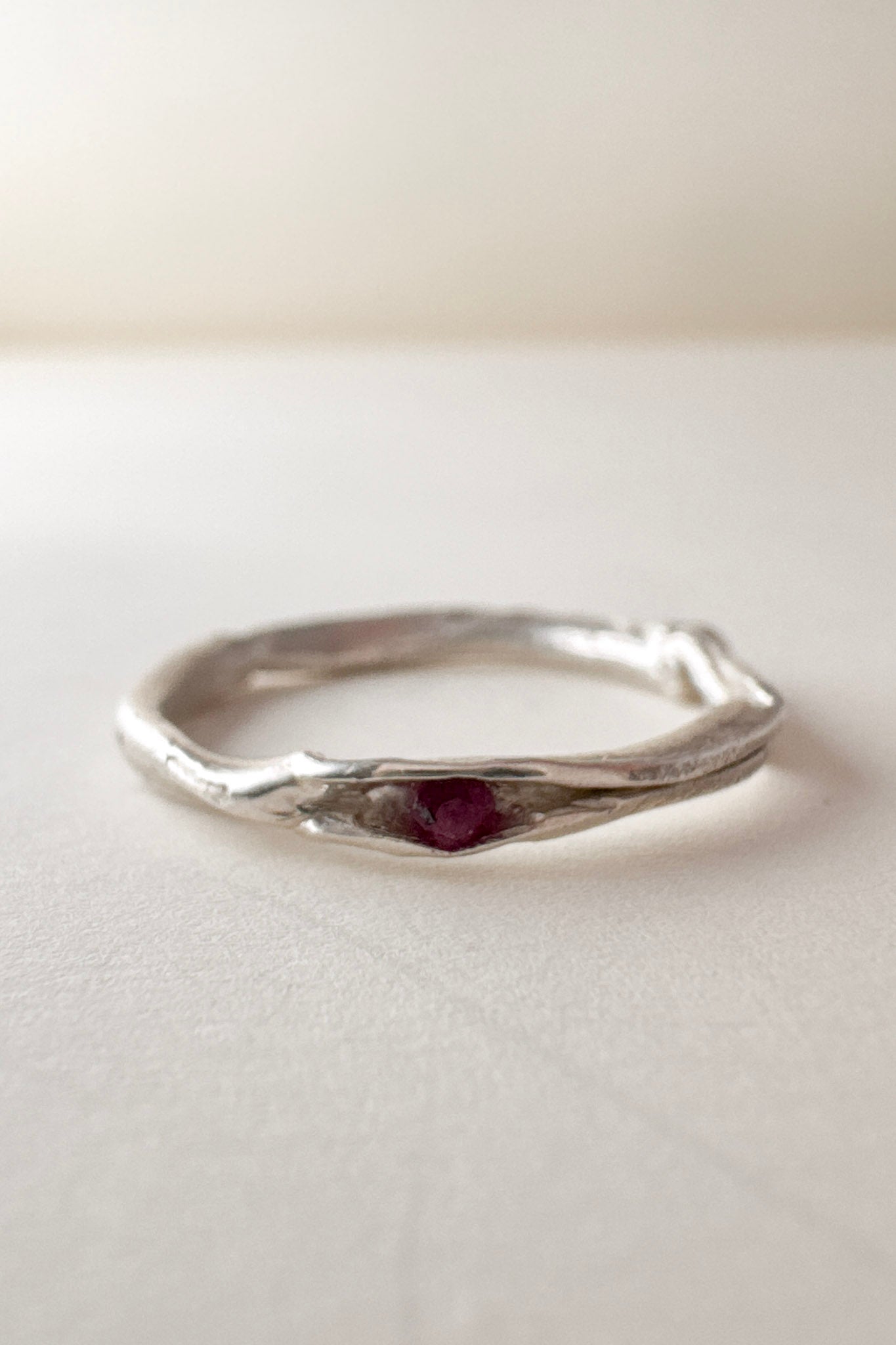 vista frontal de anillo nido, fabricado en plata con un rubí en el centro, sobre fondo claro