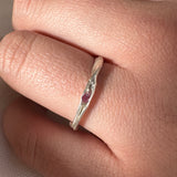 Anillo de plata con una piedra preciosa roja en un dedo sobre un fondo neutro.