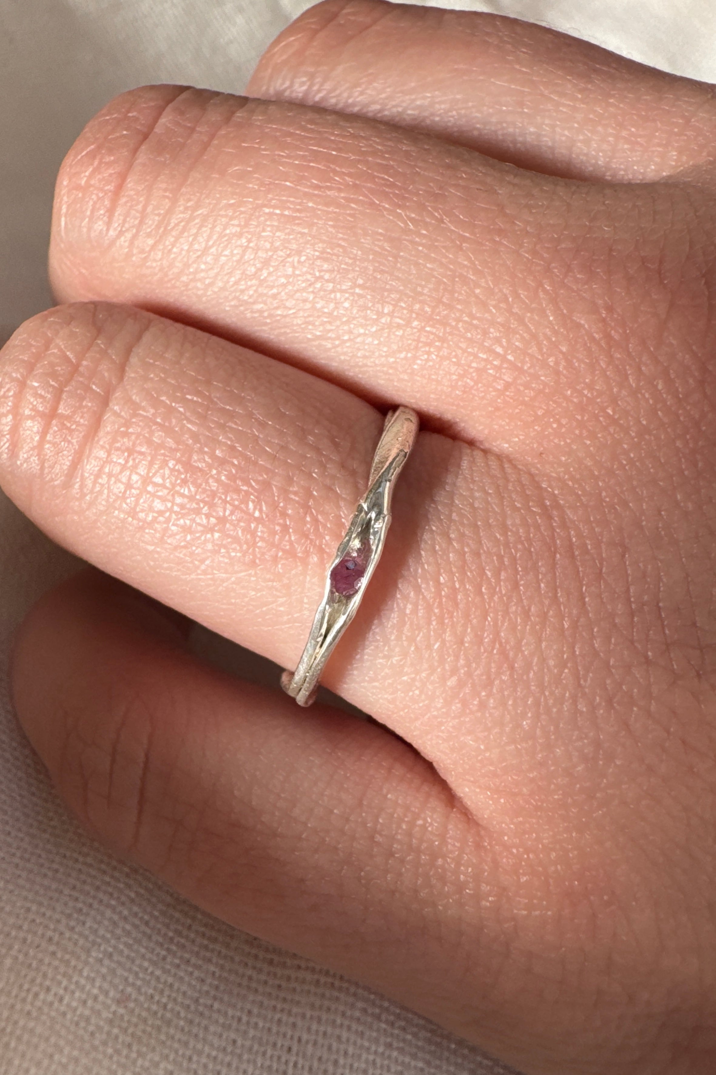 Anillo de plata con una piedra preciosa roja en un dedo sobre un fondo neutro.