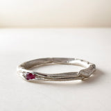 vista lateral de anillo nido, fabricado en plata con un rubí en el centro, sobre fondo claro.