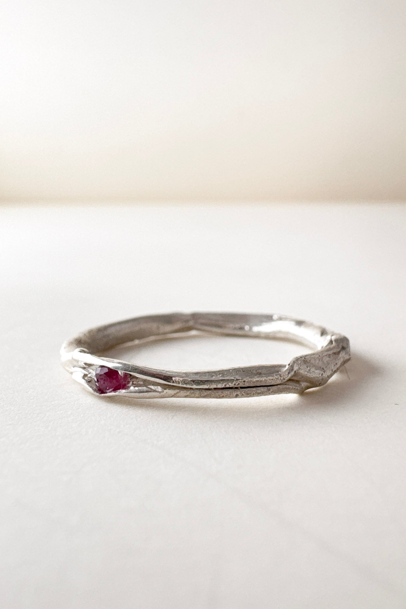 vista lateral de anillo nido, fabricado en plata con un rubí en el centro, sobre fondo claro.