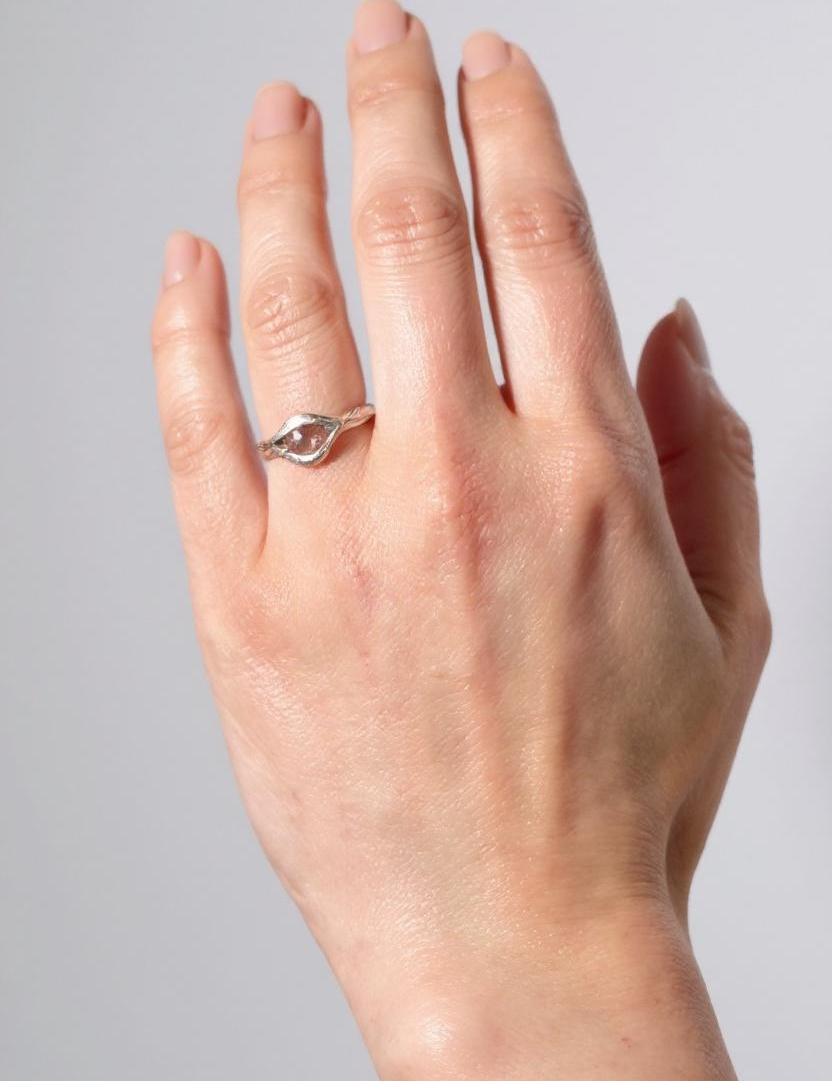 Anillo de plata esterlina con piedra del sol puesto en una mano, fotografiado sobre fondo gris claro.