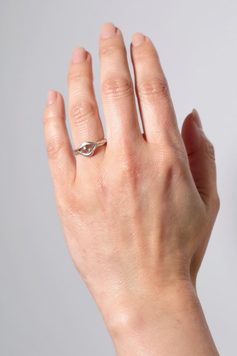 Anillo de plata esterlina con piedra del sol puesto en una mano, fotografiado sobre fondo gris claro.