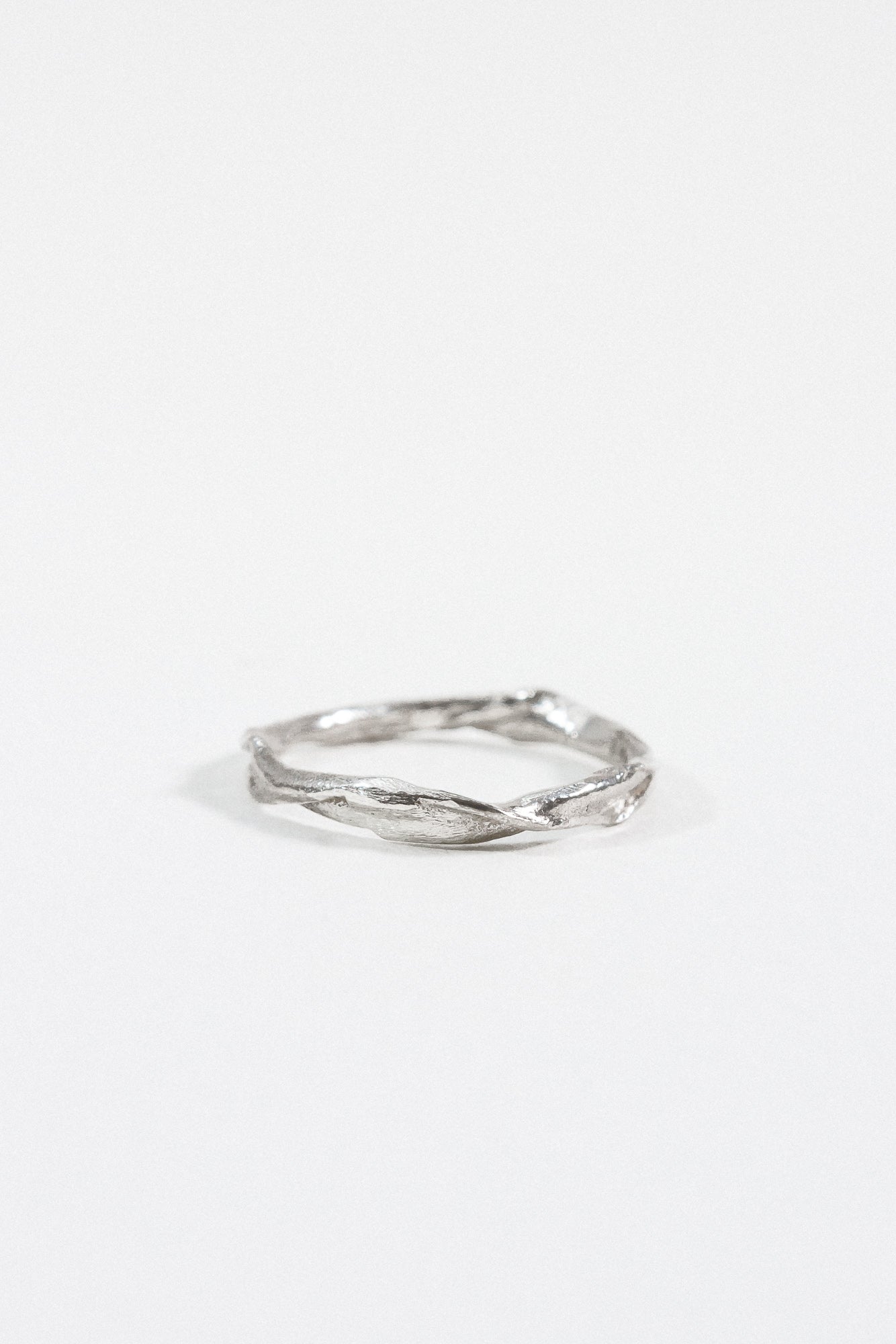 Anillo Nido Incrustado en plata esterlina con pequeño diamante de laboratorio incrustado en una banda orgánica retorcida, sobre fondo blanco.