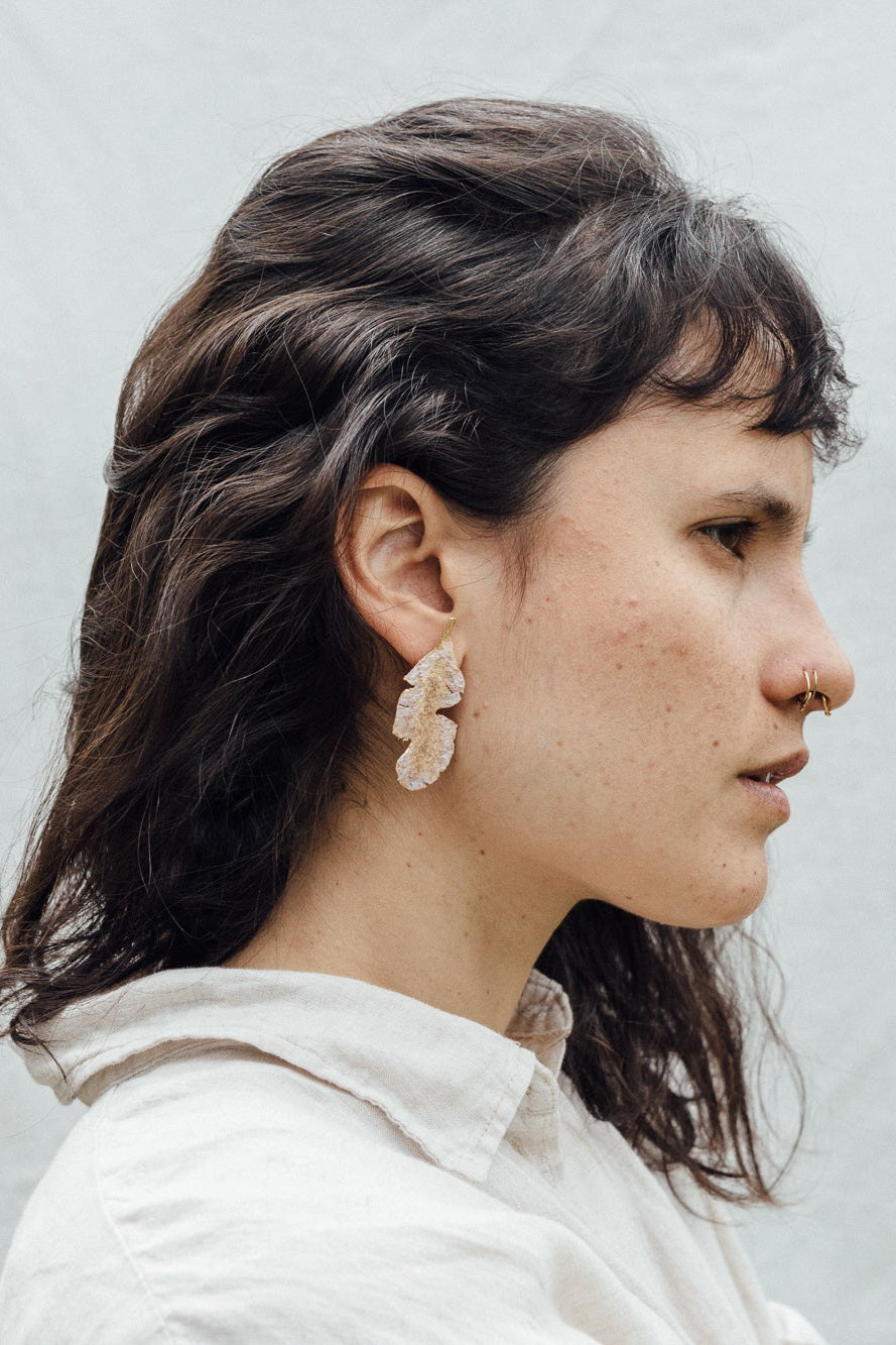 Retrato de una mujer con los aretes Hojas de Plátano—variantes pintadas a mano en verde salvia y rust con granulación de vidrio en bronce bañado en oro